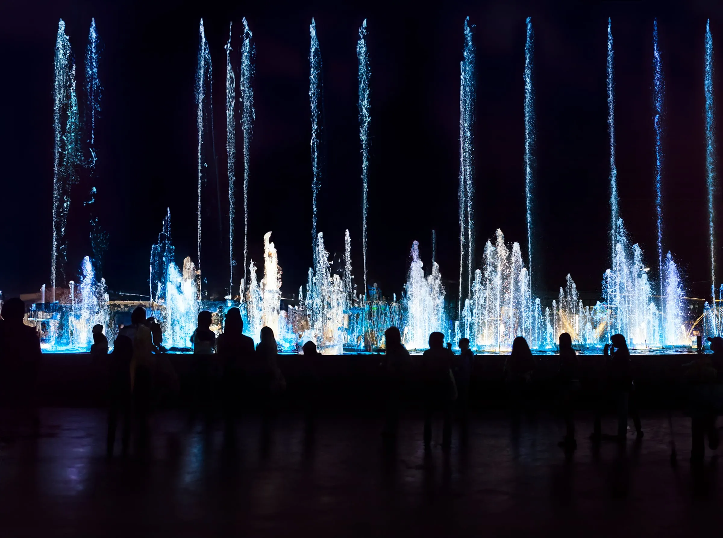 Crowd watching an illuminated AquaTronic musical fountain show at night